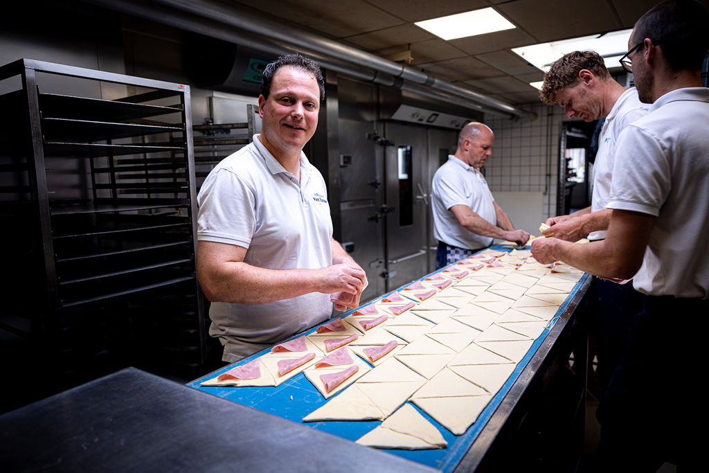 Lars en het bakkersteam vouwen saucijzenbroodjes met de hand aan de werktafel