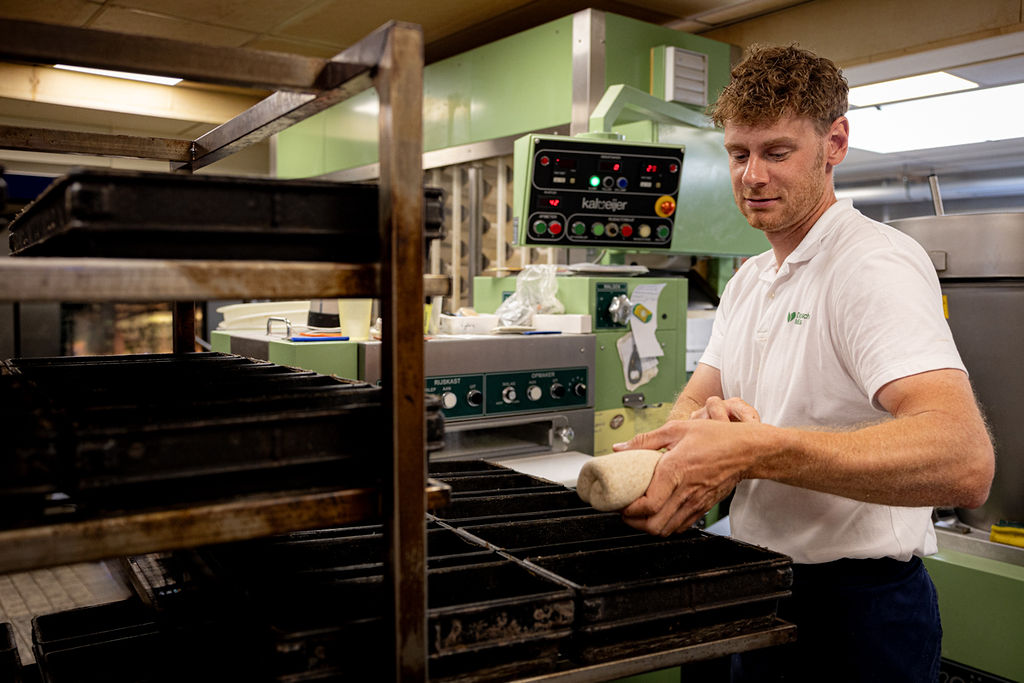 Bakker legt gevormde deegstukken in de rijskast