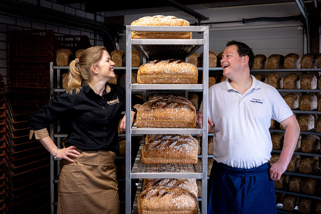 Sabine en Lars van Hassel lachend bij het rek met versgebakken meergranenbroden in de bakkerij